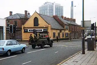 A picture of a city street with an army vehicle in the road.
