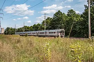 Silver single-level electric passenger train passing through grassand