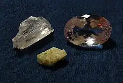 An almost colorless kunzite crystal (upper left), a cut pale pink kunzite (upper right), and a greenish hiddenite crystal (below) (unknown scale)