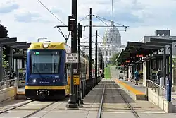 A three-car light rail at a station; the state capitol building is in the background.