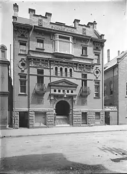 Old photo of the front of the former Hall showing its complex details. It was built of brick with a rusticated basement, balconies with curved wrought iron balustrades, a large entrance stairway under a prominent pediment and Art Nouveau panels.
