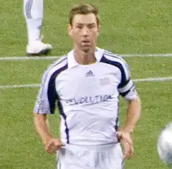 A soccer player is wearing a white New England Revolution kit and is jogging