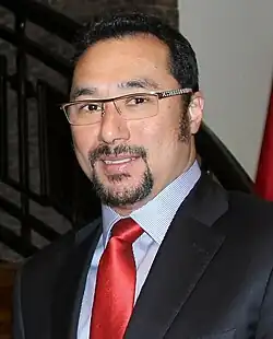 A man in a suit with black hair and glasses facing the camera