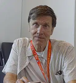 Milligan seated, wearing a lanyard and looking to the camera