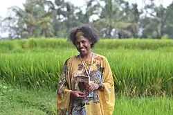 An upper body shot of woman standing in a grassy field. She is holding a copy of a novel and is smiling.