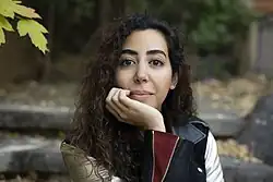 Photograph of Alsultan, a brown-skinned woman with dark curly hair, staring evenly into the camera, head on her hand