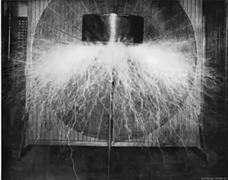 Prototype "magnifying transmitter"[18][19] in Tesla's New York lab around 1898 producing 2.5 million volts. The round "spiderweb" secondary coil is visible in background