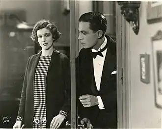 Man in tuxedo opening door to room where woman smiles back