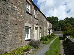 A long stone building, like a row of terraced cottages, against a background of trees.