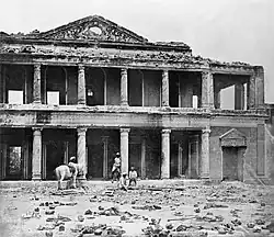 A photograph of the ruins of a palace with human skeletal remains in the foreground