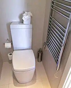 A Western flush toilet with a paper seat cover dispenser, waste basket, and toilet brush near the German-Austrian border