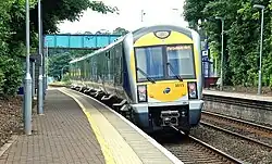 A modern train approaches the outdoor platform of a small station.
