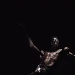 Travis Scott, shirtless, within a dark void
