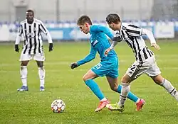 Two players with a shirt with black and white stripes and another wearing a light-blue one on playing football under the rain