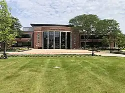 A red brick building with large windows and the text "Student Union" displayed at the top of the building. Several trees are near the building and a plaza and lawn are in front of it.