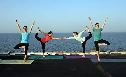 A US Navy yoga display on the flight deck of USS George H.W. Bush, using Vrikshasana and Natarajasana, 2014