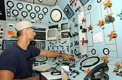 The interior of the van, showing the control panels for the saturation system and a life-support technician. Various instruments can be seen, including high precision analog pressure gauges, a telephone handset, video monitors and control valves.