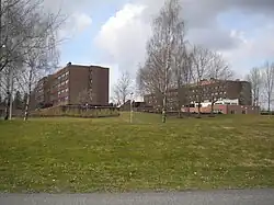 Two brown brick buildings about five floors tall and a lawn in the foreground.