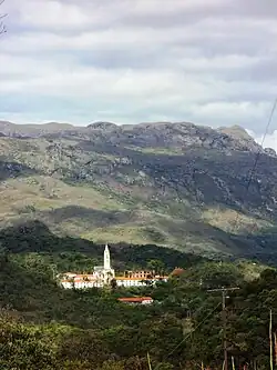 Building with tall spire nestled at the foot of a mountain range in the background