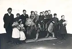 Black and white photo of children standing around and sitting on top of taxidermied lion
