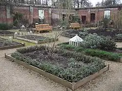 A colour photograph of the inside of a walled garden containing rectangular raised beds separated by gravel pathways