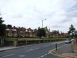 A row of small redbrick cottages with exuberant decoration to the gable ends. A central stone built hall.