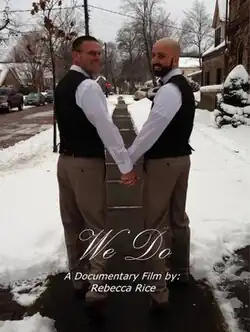 Two smiling white men wearing black vests over white shirts. They are holding hands with their bodies facing away from the viewer, though their heads are turned to face the viewer. The background is a sidewalk in winter, with snow on both sides. White text reads We Do A Documentary Film by: Rebecca Rice.