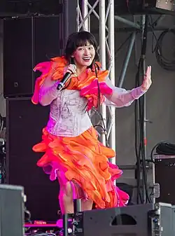 A woman wearing a white and orange dress while singing on stage