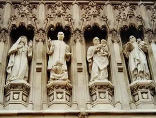 Photo shows four of ten statues above the door of the Abbey. They are carved in a realistic and lifelike manner, full of action. Elizabeth wears nun's habit and holds a cross, King preaches with a little black girl at his feet, Romero holds a naked indigenous baby, Bonhoeffer carries a book. They are set in traditional Gothic niches with ornate carved canopies.