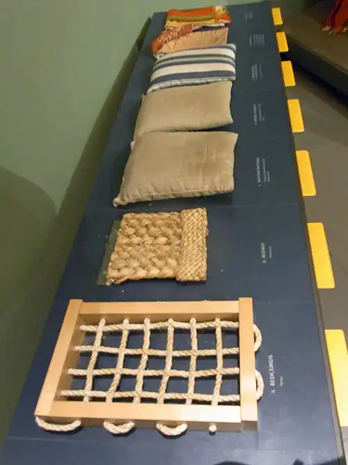 Museum samples demonstrating a 1590s bed: the bedcords, bedmat, three tick mattresses in dun and striped ticking, and the bedlinen.