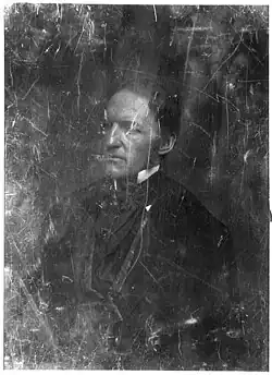 A scratched, half-length photographic portrait of a middle aged man in formal mid-19th century dress, facing left