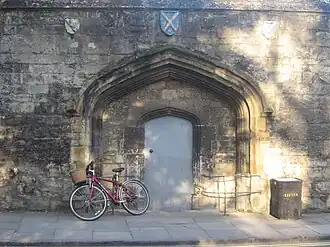 The 15th-century gate of Gloucester College, surviving to the side of the current gate and bearing the arms of the abbeys of Winchcombe, St Albans and Ramsey