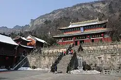 A Chinese temple with a prominent staircase in front and a hill in the background