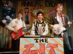 Three young men with musical instruments performing on stage. On the left is the bassist, in the centre is the keyboardist, and on the right is the guitarist.