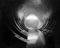 Black and white image of Hoover Dam with the following printed description: "View of 50-foot diameter tunnel below Arizona Tunnel Plug outlet works with Stoney Gate at end of tunnel lowered."