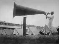 A sailor using a megaphone to amplify the sound of a bugle to wake recruits at an American training camp in 1947